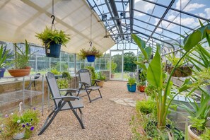 A greenhouse with hanging planters, a table with chairs, and a variety of plants. - Private Pool & Hot Tub | Fall color view for miles (Eureka Springs)