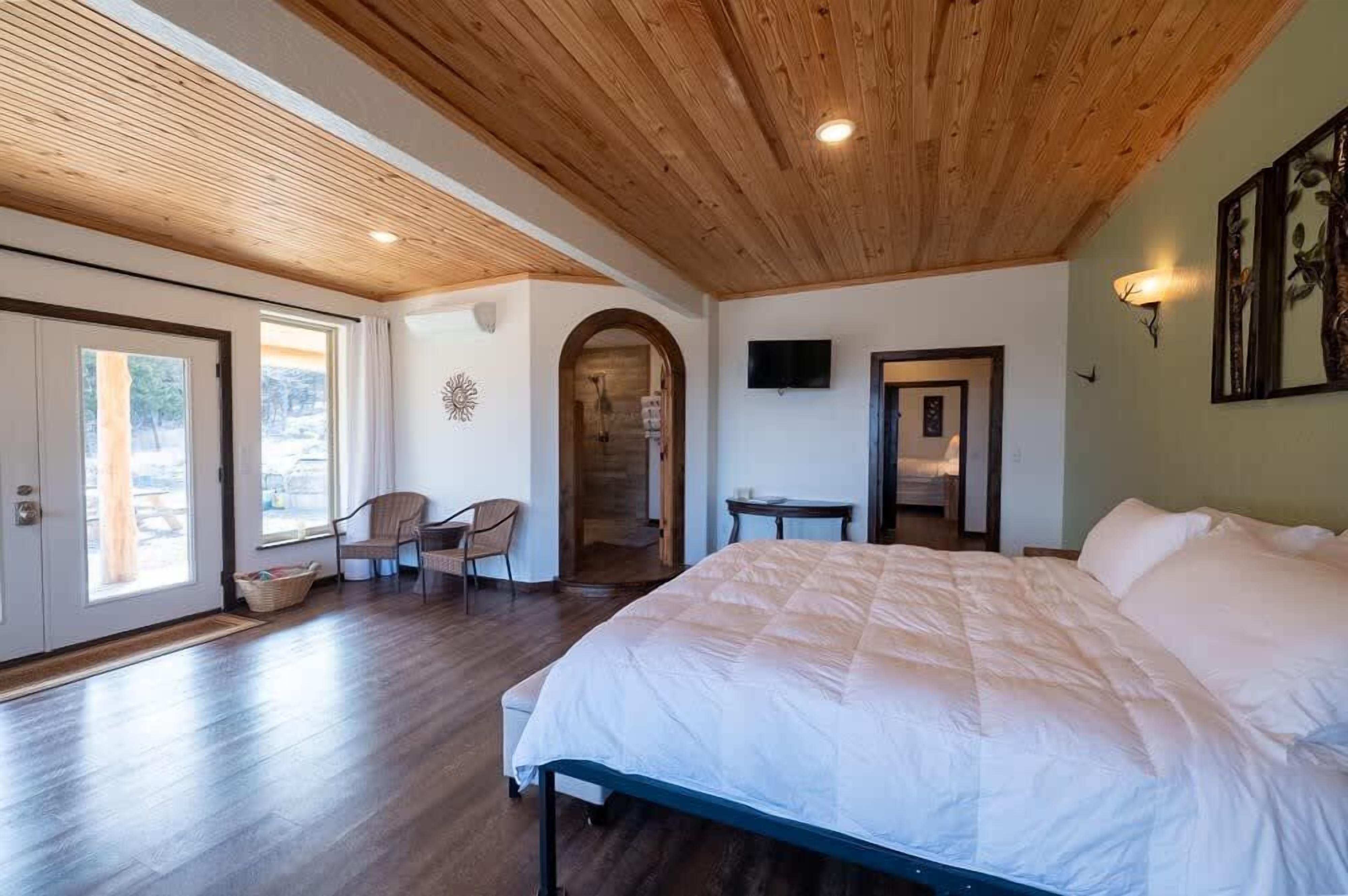 Une chambre avec un grand lit, un plafond en bois et un téléviseur fixé au mur.