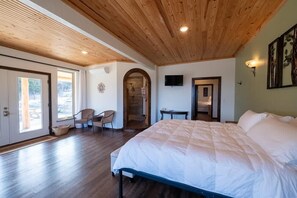 A bedroom with a large bed, wooden ceiling, and a TV on the wall. - Private Pool & Hot Tub | Fall color view for miles (Eureka Springs)