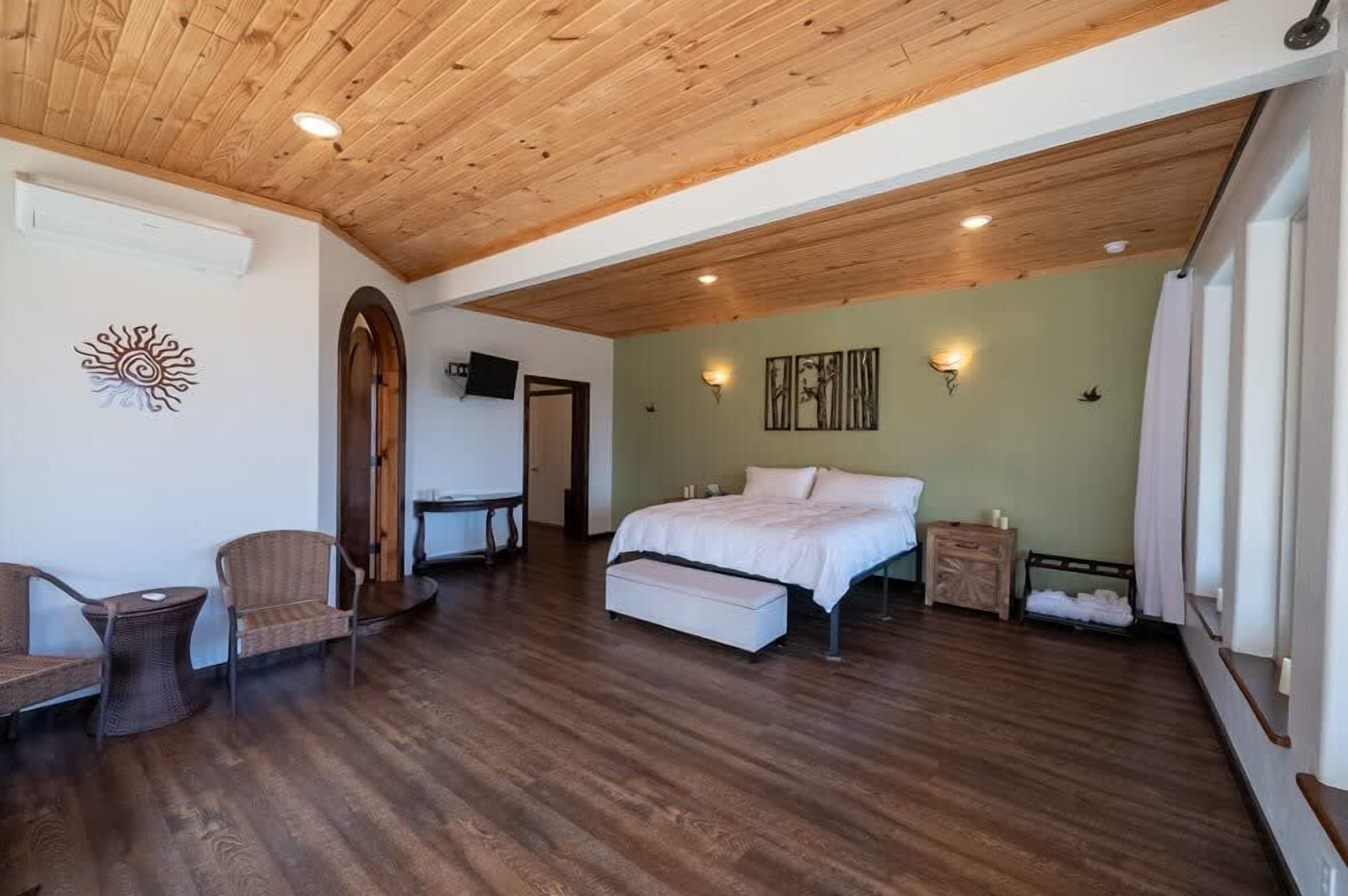 A spacious bedroom with a wooden ceiling, a bed, a small table, and a chair.