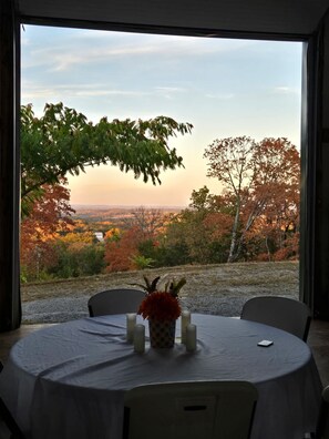 Uma mesa com um vaso de flores e velas, com vista para uma paisagem arborizada e um horizonte distante.
