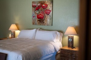 Un lit bien fait, avec du linge de lit blanc, deux lampes de chevet et un tableau représentant des fleurs rouges accroché au mur.