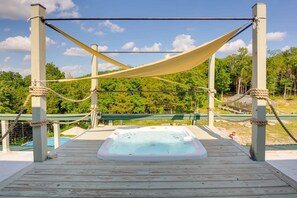 Un bain à remous sur une terrasse en bois, entouré d’une barrière en corde et surmonté d’un auvent.