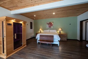 A bedroom with a wooden ceiling, a bed with white bedding, two bedside lamps, and a wooden bench.