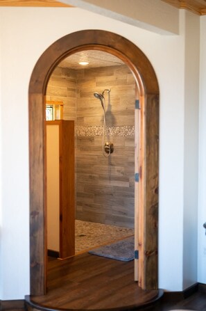 An arched doorway leading to a shower area with wooden flooring and a tiled wall.