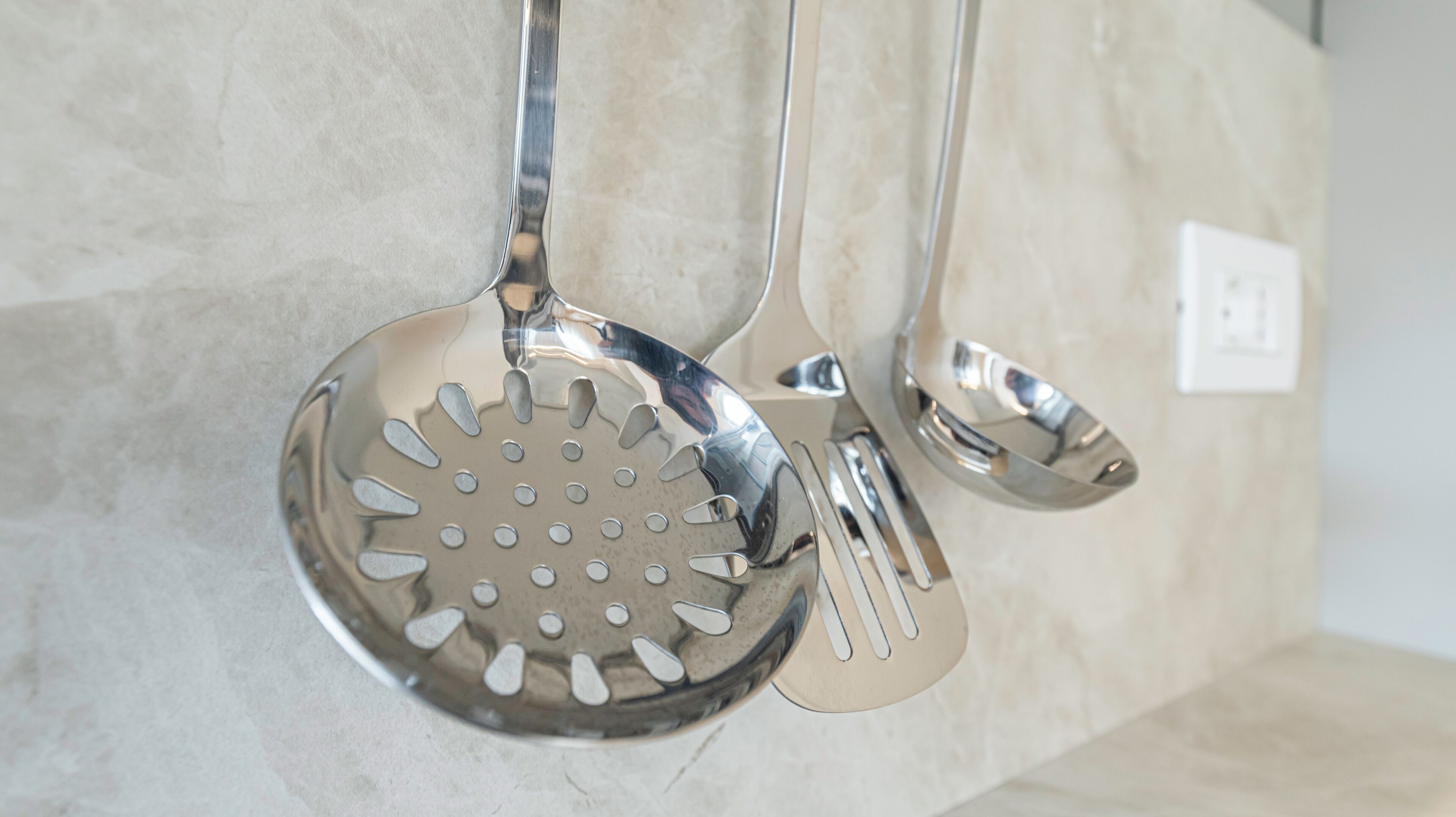 Un ensemble d’ustensiles de cuisine comprenant une passoire, une écumoire et une spatule, le tout accroché au mur.