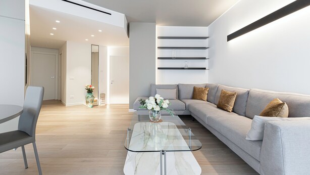 A modern living room with a grey sofa, a glass coffee table, and a vase of white flowers. - Italianway - Transiti 20 (Milan)