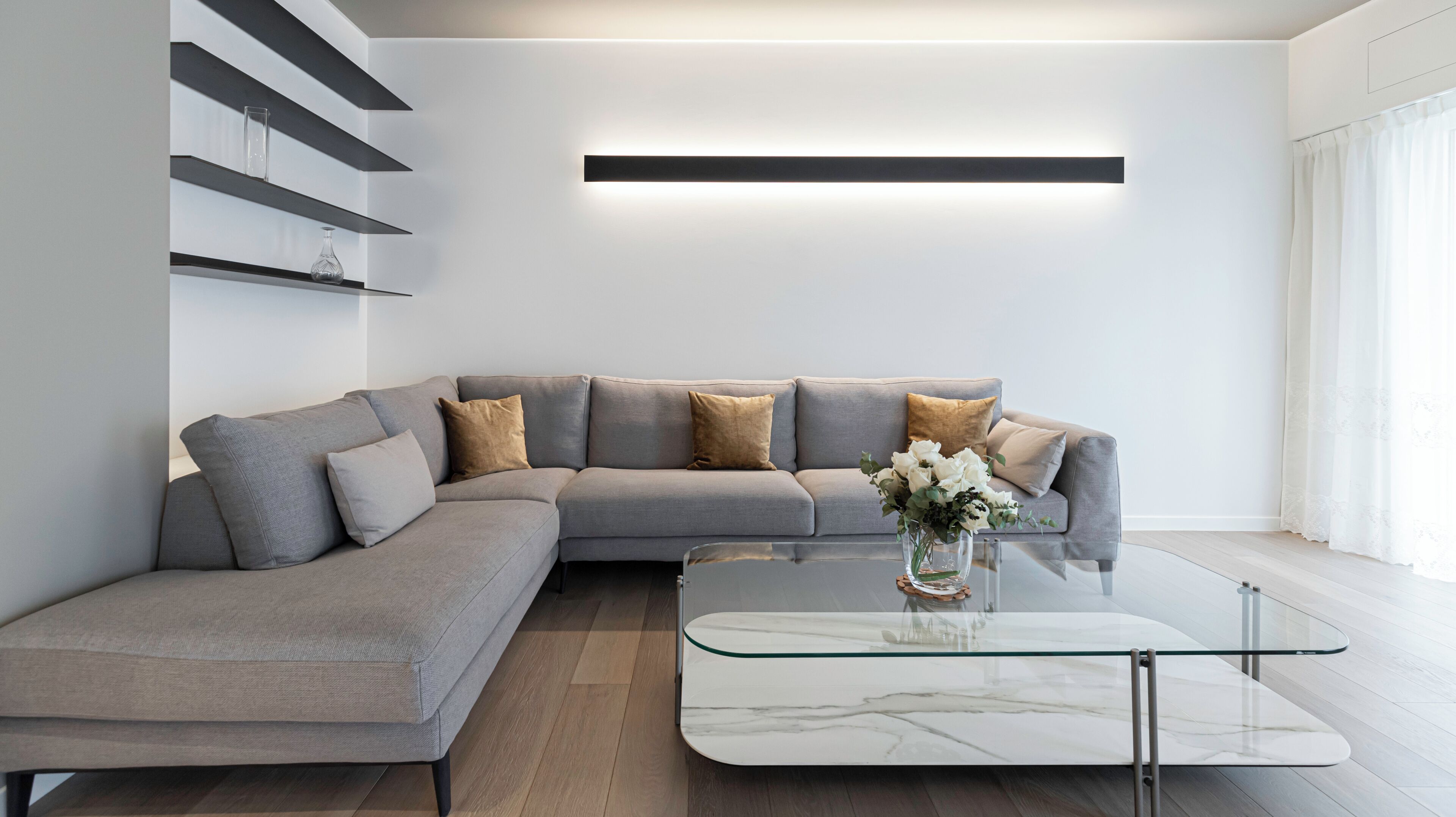 Una sala de estar moderna con un sofá seccional gris, una mesa de centro de vidrio y un diseño minimalista.