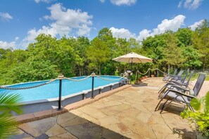 Piscina com barreira de corda, rodeada por espreguiçadeiras e um guarda-sol, com um cenário de vegetação exuberante.