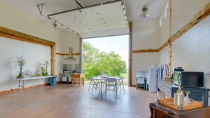 A spacious room with a large table and chairs, a kitchen area, and a view of greenery outside.