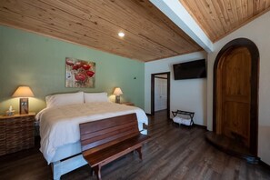 A bedroom with a wooden bed, two bedside lamps, a mounted TV, and a wooden door.