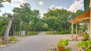 A gravel driveway leading to a wooden structure with a covered porch, surrounded by lush greenery and trees.