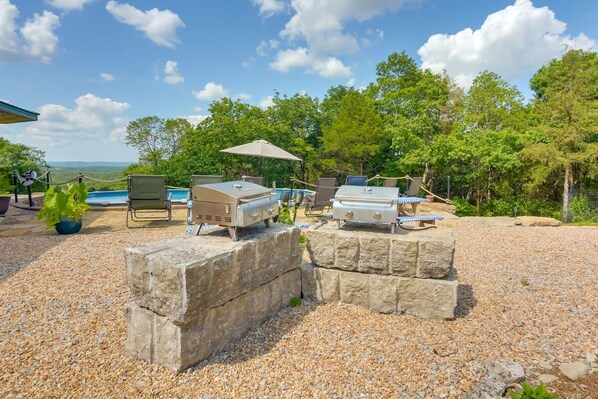 Un espace barbecue extérieur agrémenté de structures en pierre, d’une piscine et offrant une vue sur le paysage.