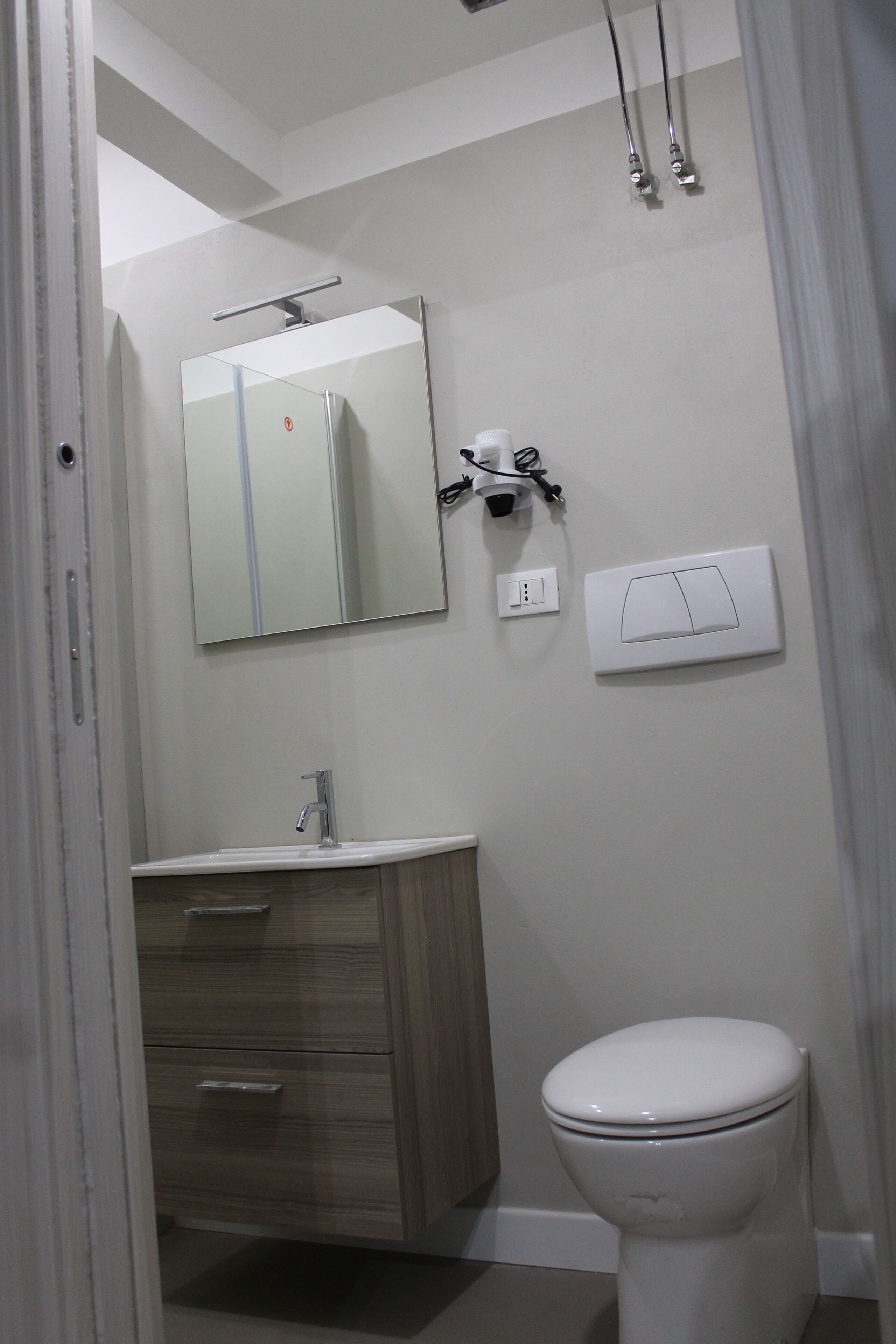 Ein Badezimmer mit Toilette, Waschbecken mit Spiegel darüber und Duschkopf.