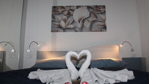 A hotel room with a bed, a heart-shaped towel arrangement, and a floral wall art piece. - B&B Vista Normanna (Pietramontecorvino)