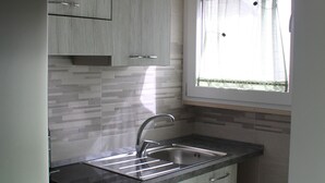 A compact kitchen with light wood cabinets, a stainless steel sink, and a window with sheer curtains. - B&B Vista Normanna (Pietramontecorvino)