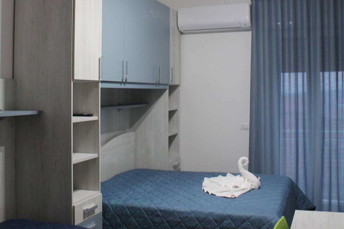 A bedroom with two beds, a desk, a wardrobe, and an air conditioning unit.