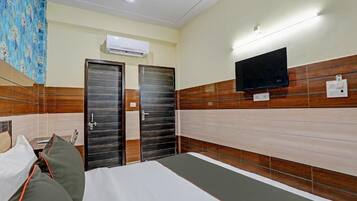 Habitación de hotel con cama, dos puertas, un televisor montado y un equipo de aire acondicionado.