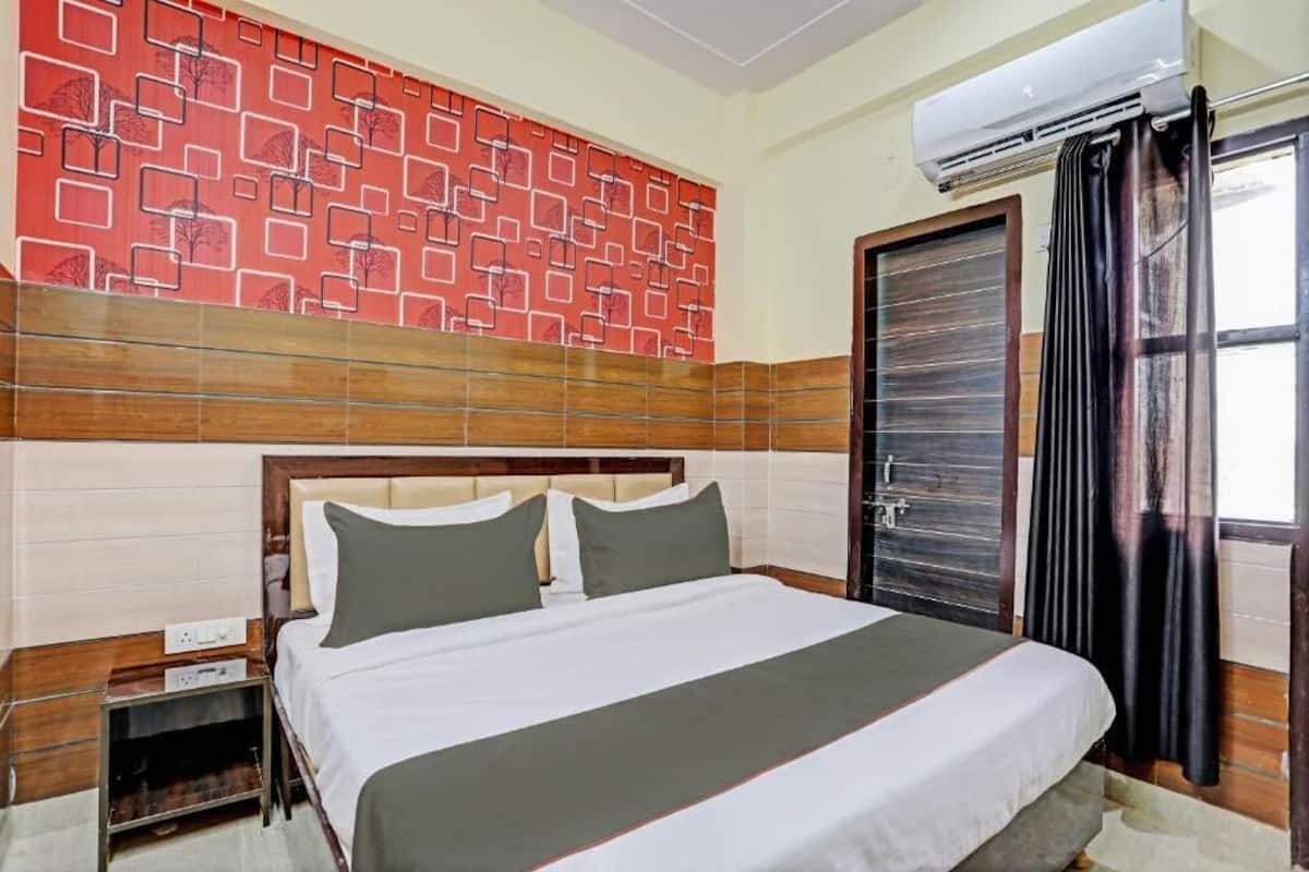 Una habitación de hotel con cama, mesita de noche, pared con diseño geométrico, unidad de aire acondicionado y puerta con cortinas.