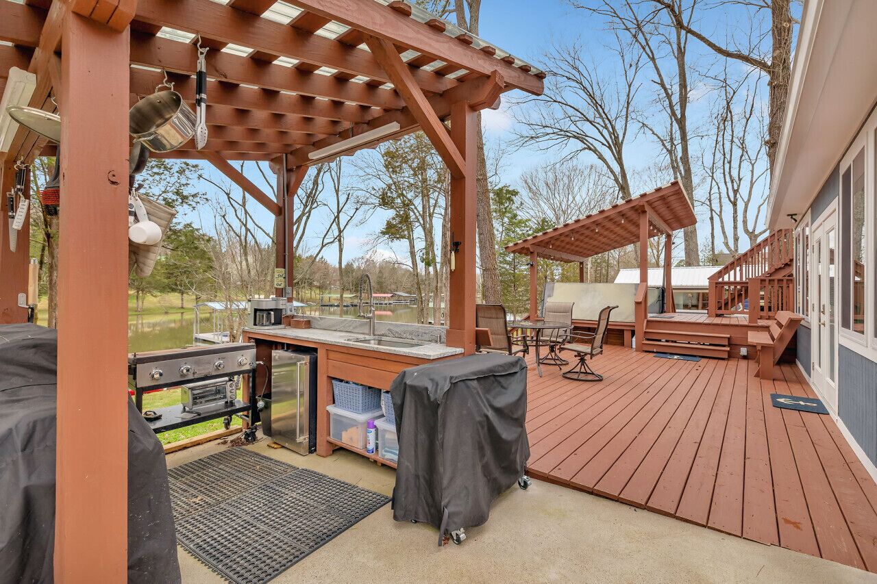 A covered outdoor deck with barbecue equipment, seating, and a pergola structure.