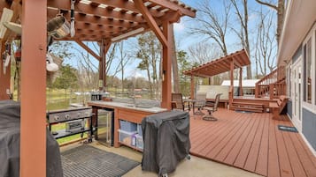 A covered outdoor deck with barbecue equipment, seating, and a pergola structure.