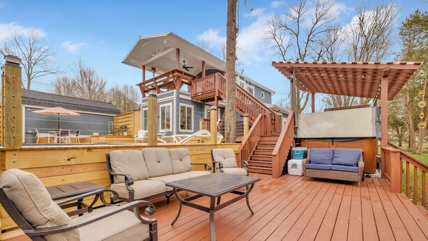 A wooden deck with outdoor furniture, a covered seating area, and a staircase leading to an upper level.