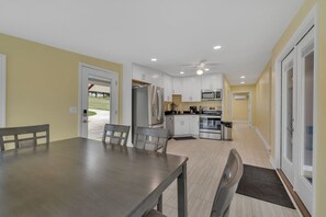 A modern kitchen with white cabinets, stainless steel appliances, and a dining area with a wooden table and chairs. - Lakefront, Heated Pool, Sauna, Sleeps 8! (Lebanon)