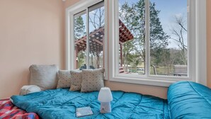 A bedroom with a large window, a bed with blue bedding, and a view of the outdoors.