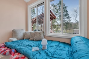 Une chambre avec une grande fenêtre, un lit avec une literie bleue et une vue sur l’extérieur.