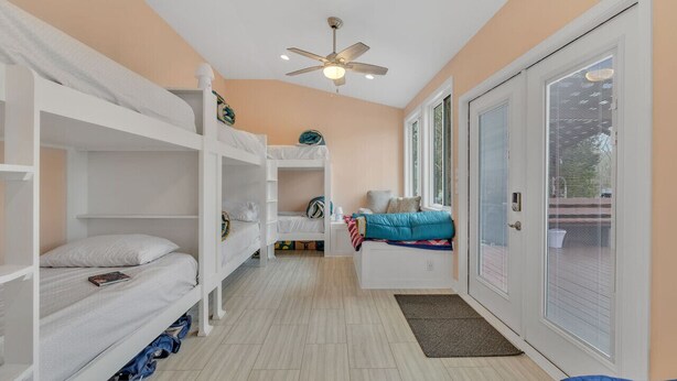 Une chambre avec des lits superposés, un ventilateur de plafond et une porte-fenêtre coulissante donnant sur un espace extérieur.
