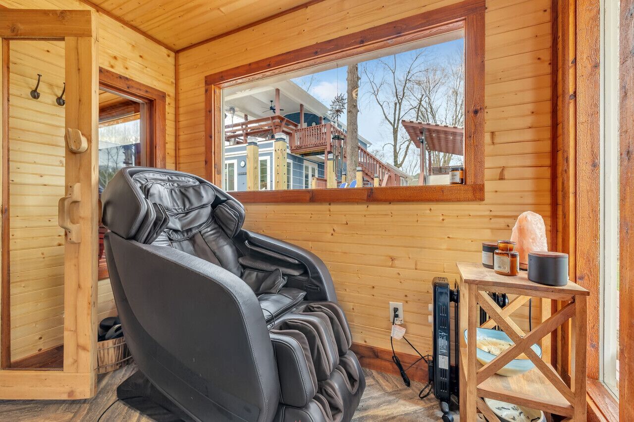 A massage chair in a wooden cabin with a view of a house through a window.
