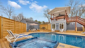 A backyard with a hot tub, a wooden deck, a pool, and a covered patio area.