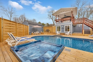 Un jardin avec un jacuzzi, une terrasse en bois, une piscine et un patio couvert.
