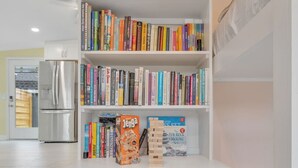 Un espace de vie compact comprenant un coin cuisine, une bibliothèque remplie de livres et un petit réfrigérateur.