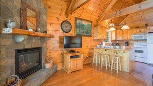 Een houten cabin met een stenen openhaard, houten planken, een televisie, een keukenhoek en een barkruk.
