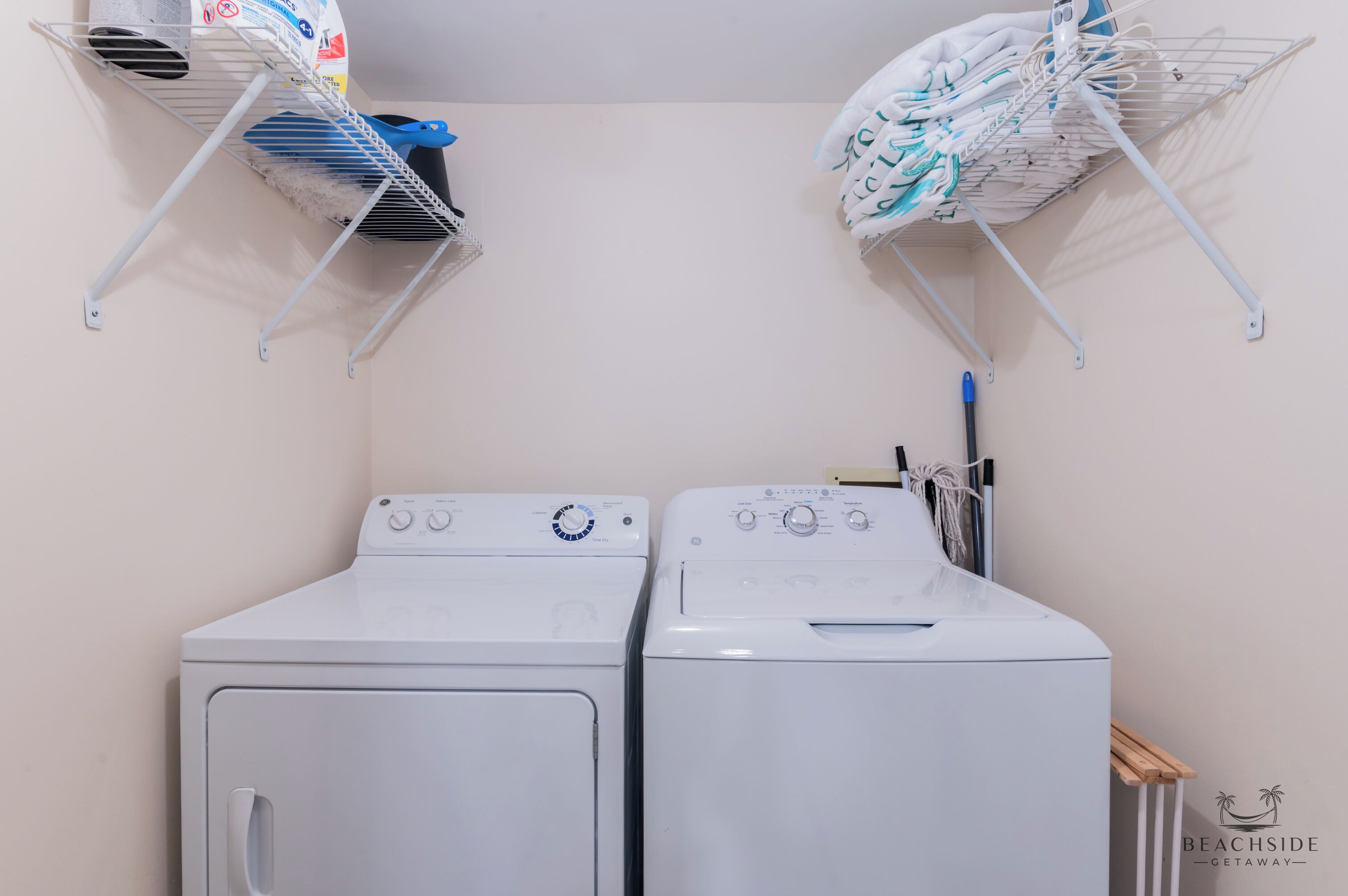 A laundry area with two white washing machines and two metal drying racks with folded clothes.