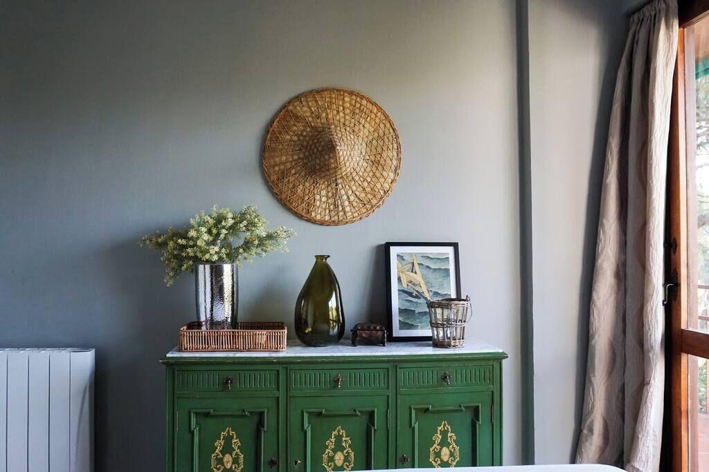 Un mobiletto verde con oggetti decorativi, tra cui un cesto intrecciato, un vaso con fiori e un quadro incorniciato.