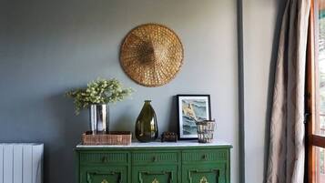 Un mobiletto verde con oggetti decorativi, tra cui un cesto intrecciato, un vaso con fiori e un quadro incorniciato.