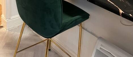 A kitchen with a green chair, a white kettle, and a marble countertop.