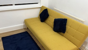 A yellow sofa with two dark blue pillows, a dark blue rug, and a white radiator. - Leicester Aprt-sleeps3-db-tv-wifi (Leicester)