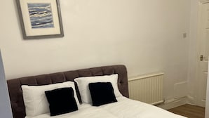 A neatly made bed with white bedding and two black pillows, a framed picture on the wall, and a white door in the background. - Leicester Aprt-sleeps3-db-tv-wifi (Leicester)