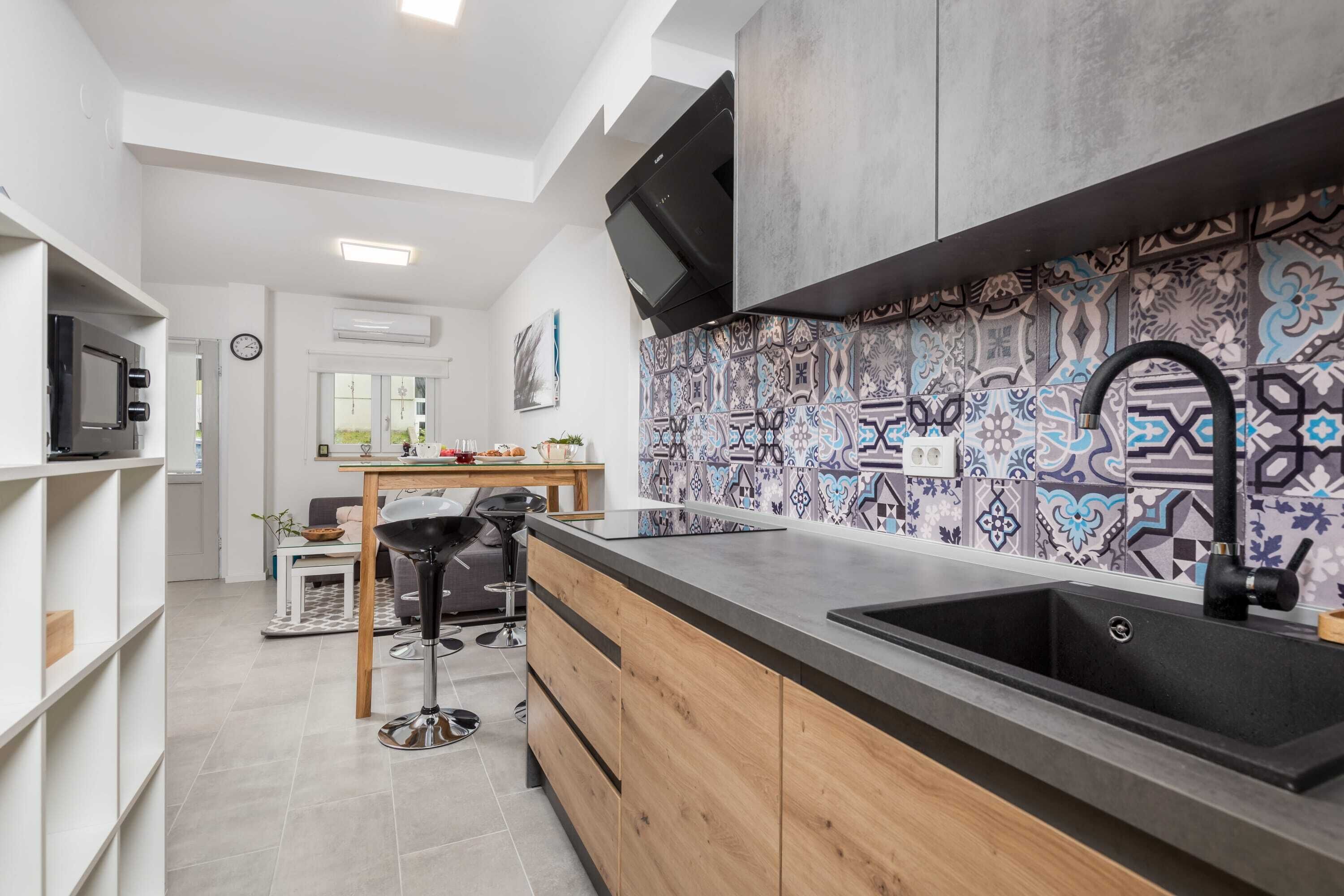 Una cocina moderna con un lavamanos negro, armarios de madera y azulejos decorativos en la pared.