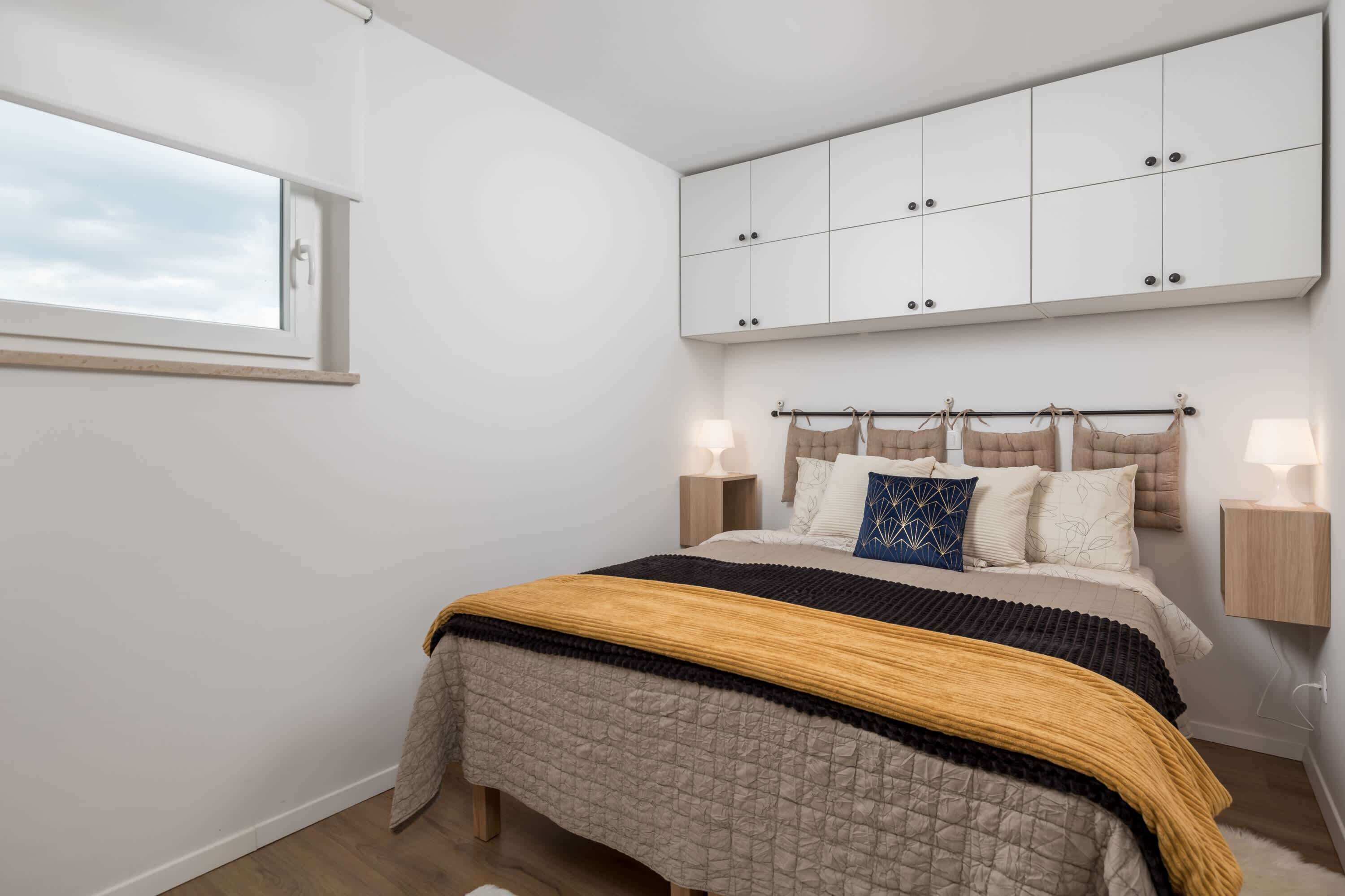 A bedroom with a bed, a window, a wardrobe, and bedside lamps.