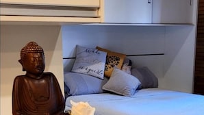 A bedroom with a white bed, a small table with a Buddha statue and a vase of flowers, and a wooden ceiling. - Lovely 1-bed Chalet in Mutari/santa Cruz Cabralia (Santa Cruz Cabralia)