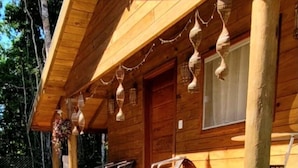 A wooden cabin with a porch, outdoor seating, and a garden with a single flower. - Lovely 1-bed Chalet in Mutari/santa Cruz Cabralia (Santa Cruz Cabralia)