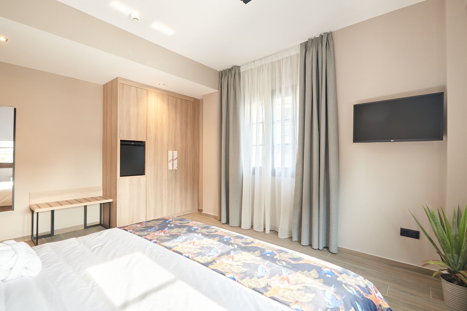 A modern bedroom with a bed, a bench, a TV, and a potted plant.