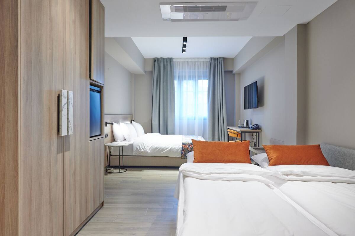 A hotel room with a bed, a desk, a chair, a TV, and a window with curtains.