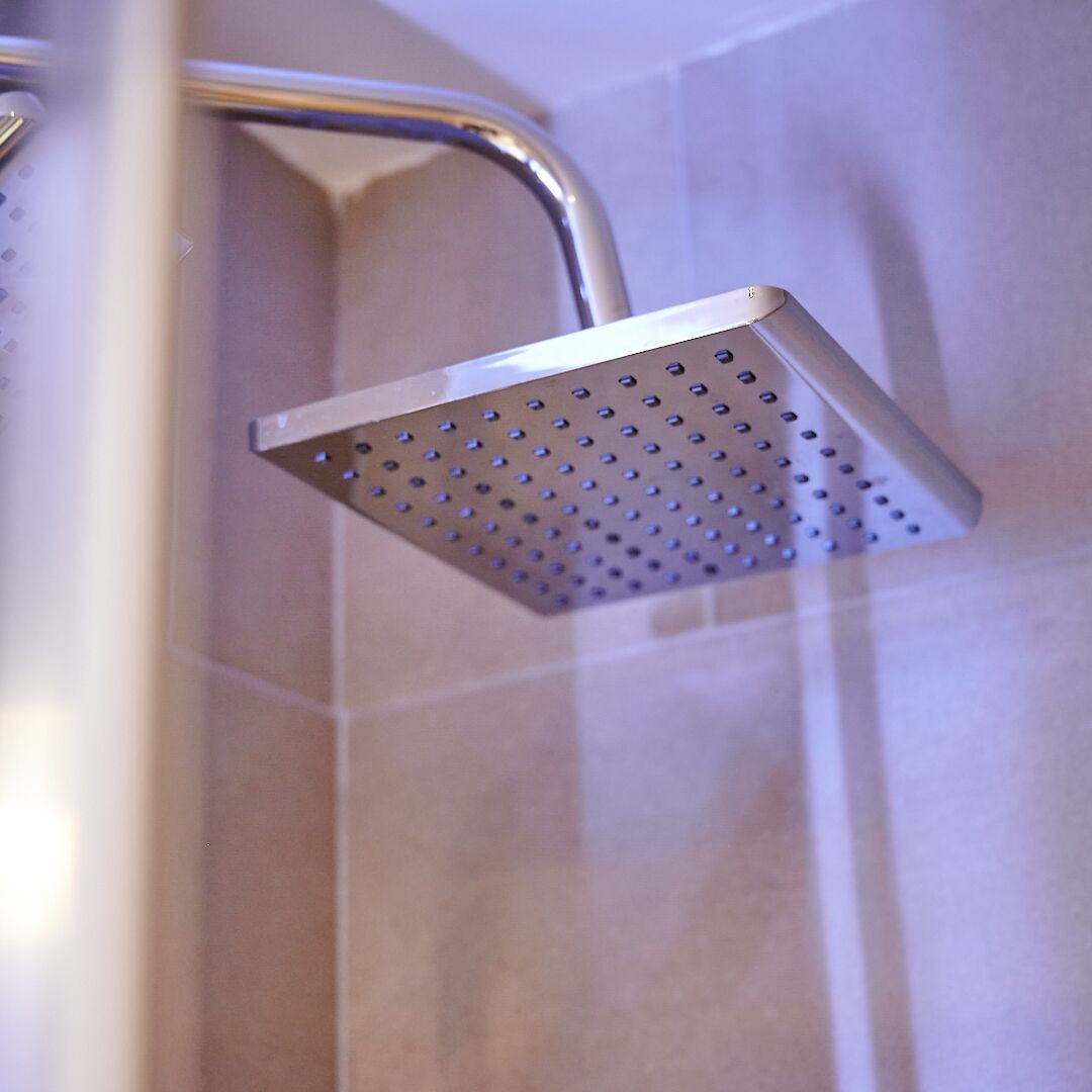 A showerhead with a perforated design, mounted on a wall with a tiled surface.