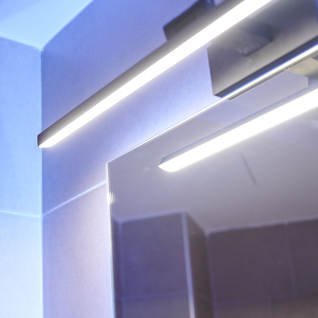 A modern bathroom with a sleek design, featuring a large mirror and a linear light fixture.