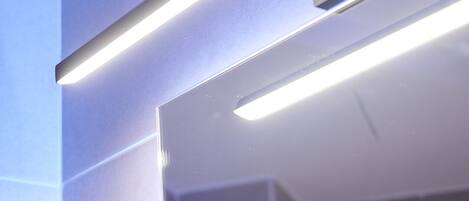 A modern bathroom with a sleek design, featuring a large mirror and a linear light fixture.
